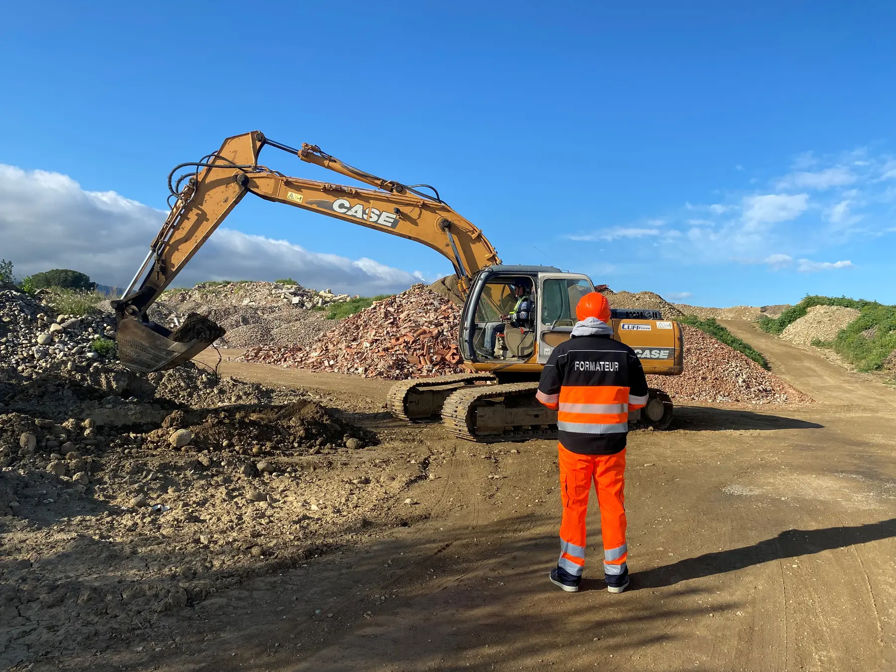 Un formateur de FormaSud Conseil au pied d'une pelle hydraulique sur la piste extérieure